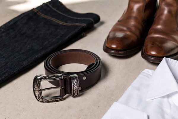 Editorial scene of a leather belt with a cowboy-style buckle styled with denim and boots