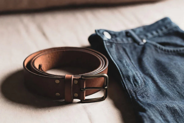 Editorial workwear scene with a casual leather belt beside denim and cotton trousers