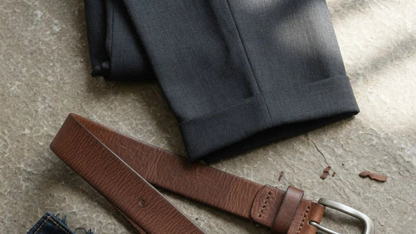 Editorial flat lay of a full grain leather belt styled with tailored trousers and denim