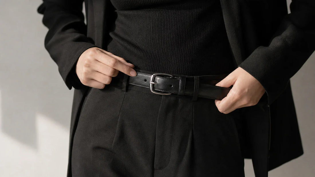 Woman styling a black leather belt with silver hardware in a dark tailored outfit