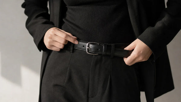 Woman styling a black leather belt with silver hardware in a dark tailored outfit