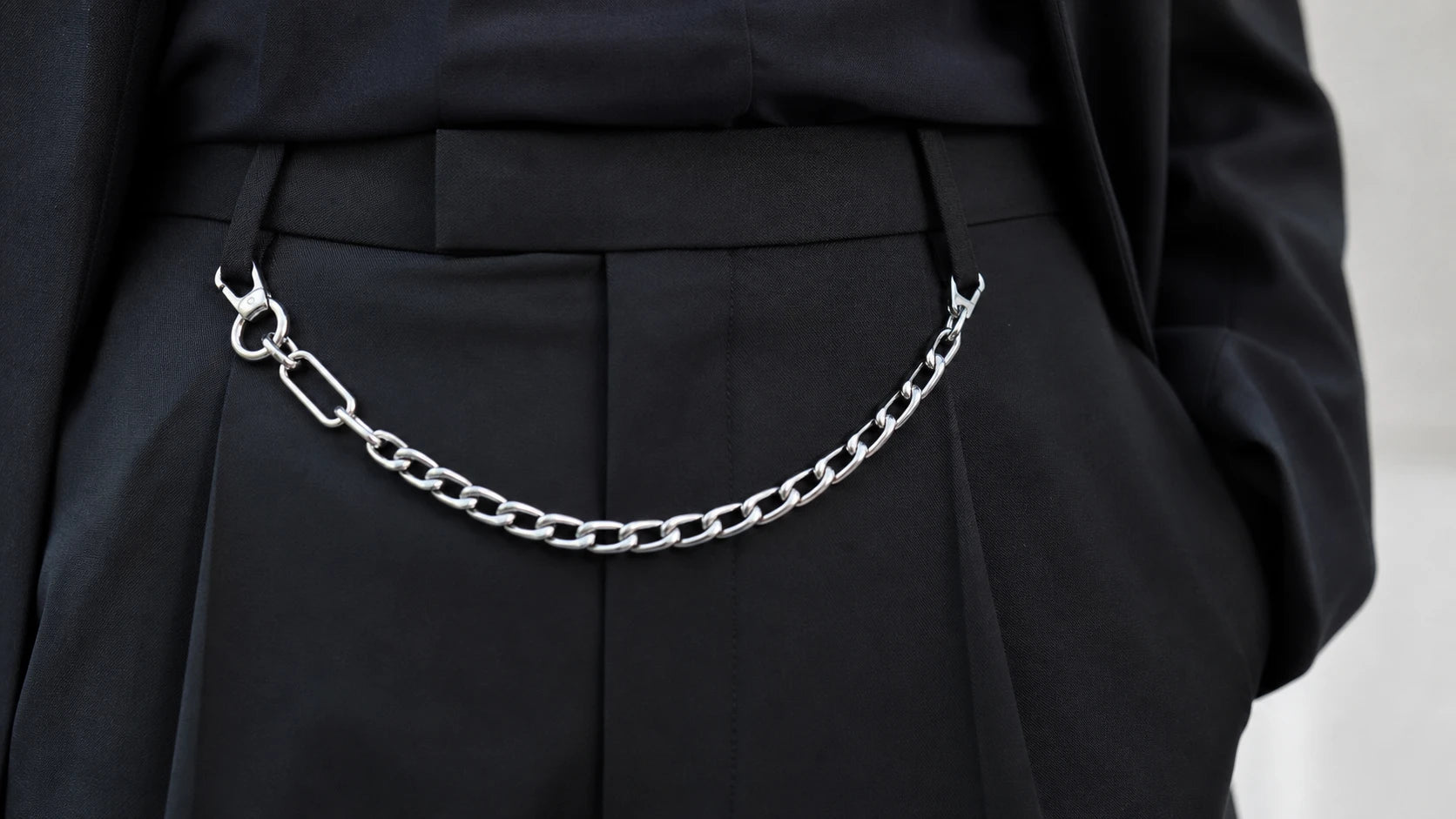 Close-up of a silver chain belt sitting neatly on a structured trouser waistband